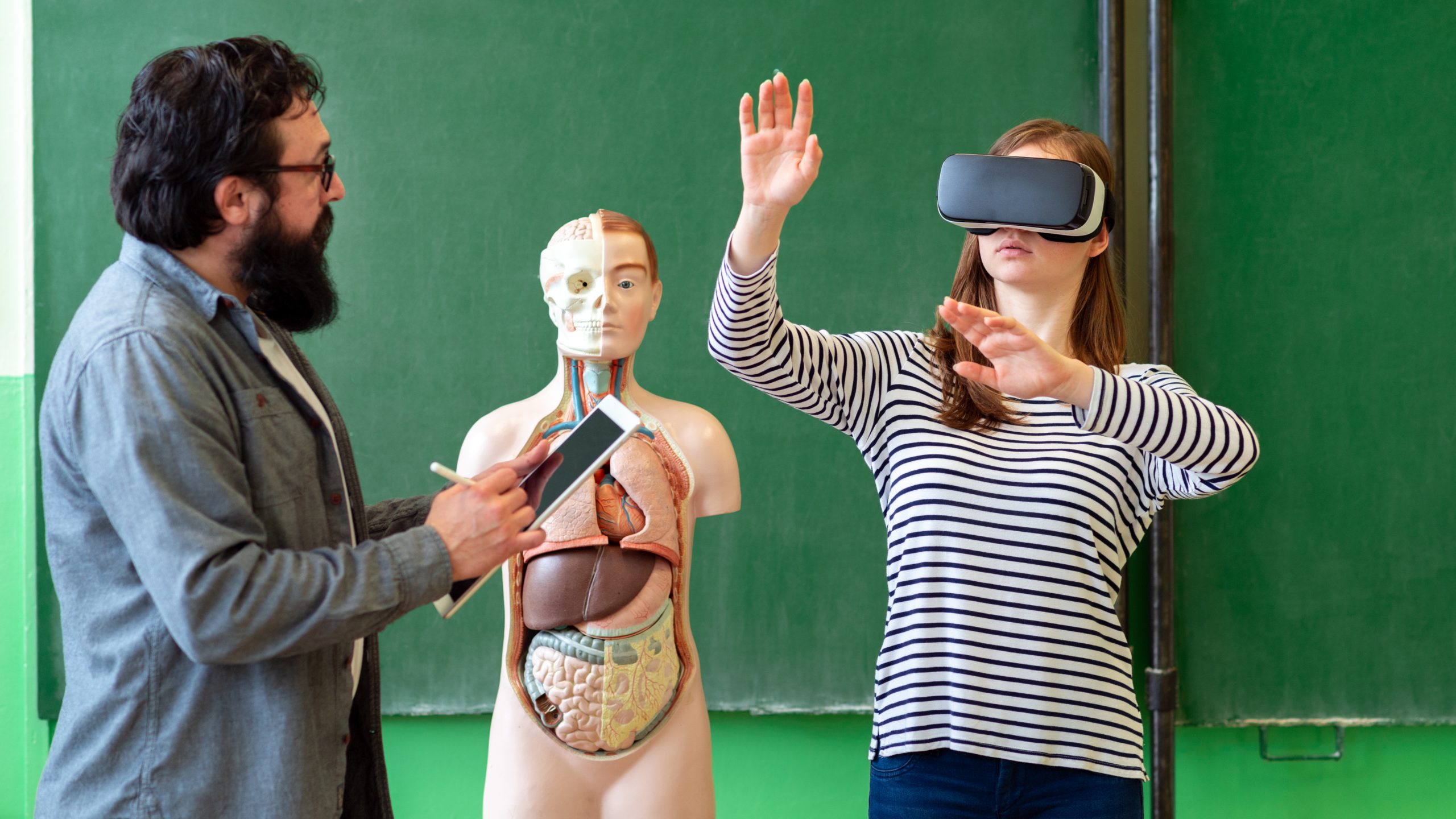 Young teacher employing Virtual Reality Glasses during a 3D biology presentation to engage students, showcasing modern teaching methods and technologies.