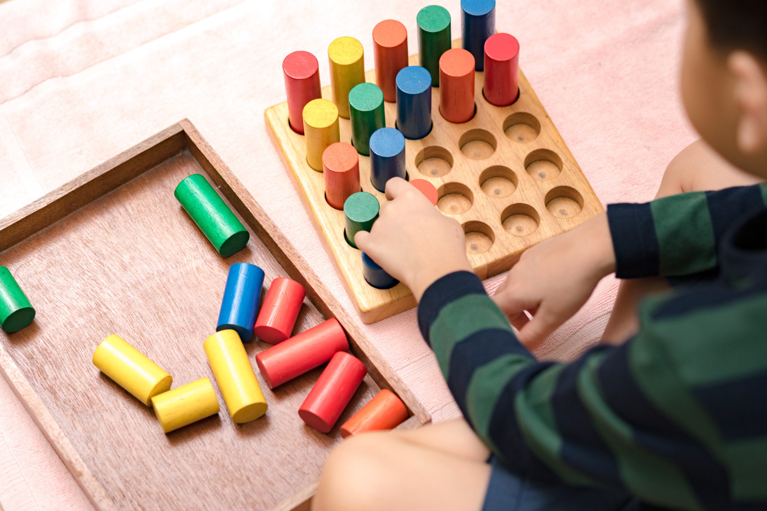 Child's hands engaging with colorful wooden Montessori sensorial blocks, demonstrating learning about size and order.