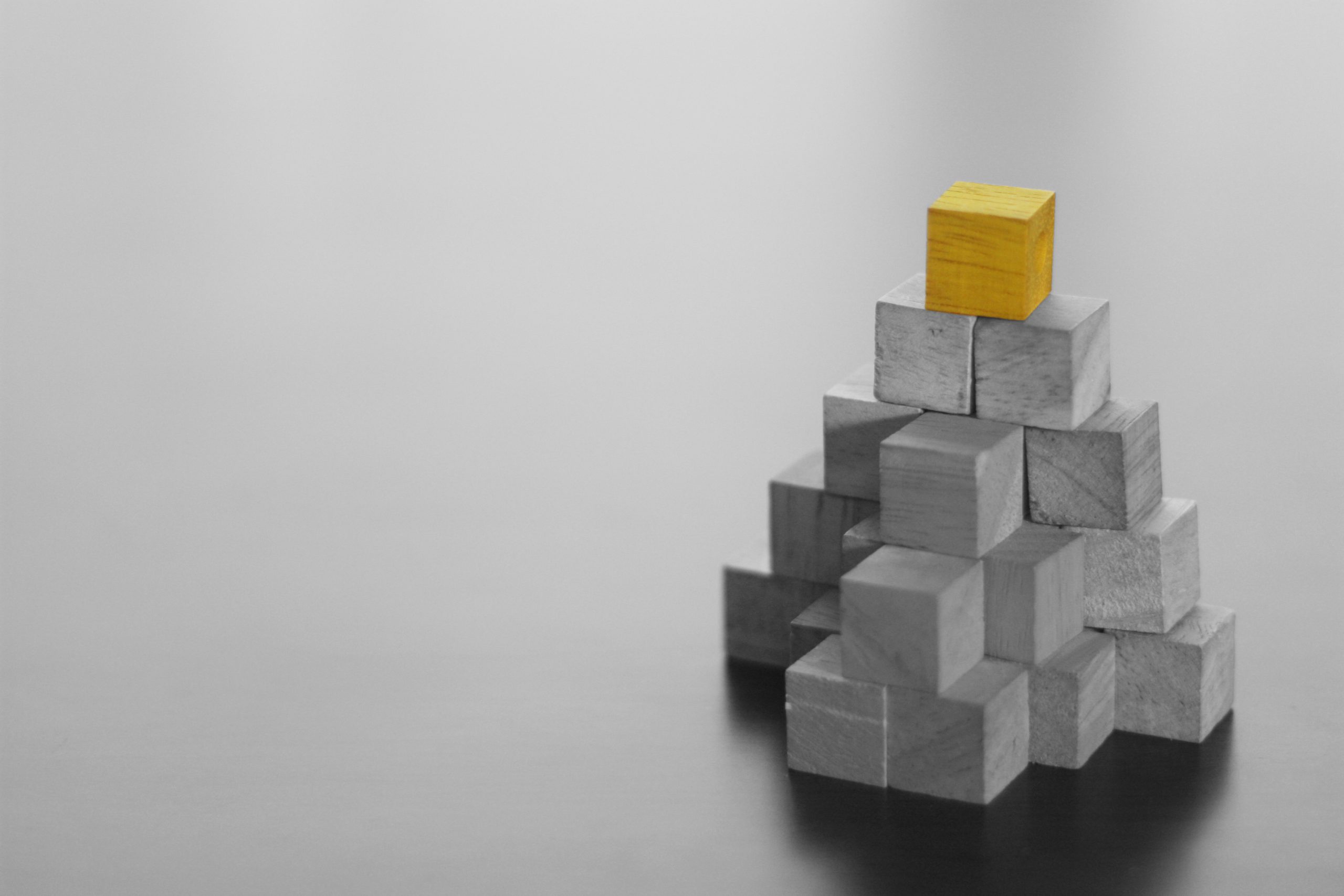 Gold cube placed on the pinnacle of a wooden pyramid, symbolising the achievement of self-actualisation.