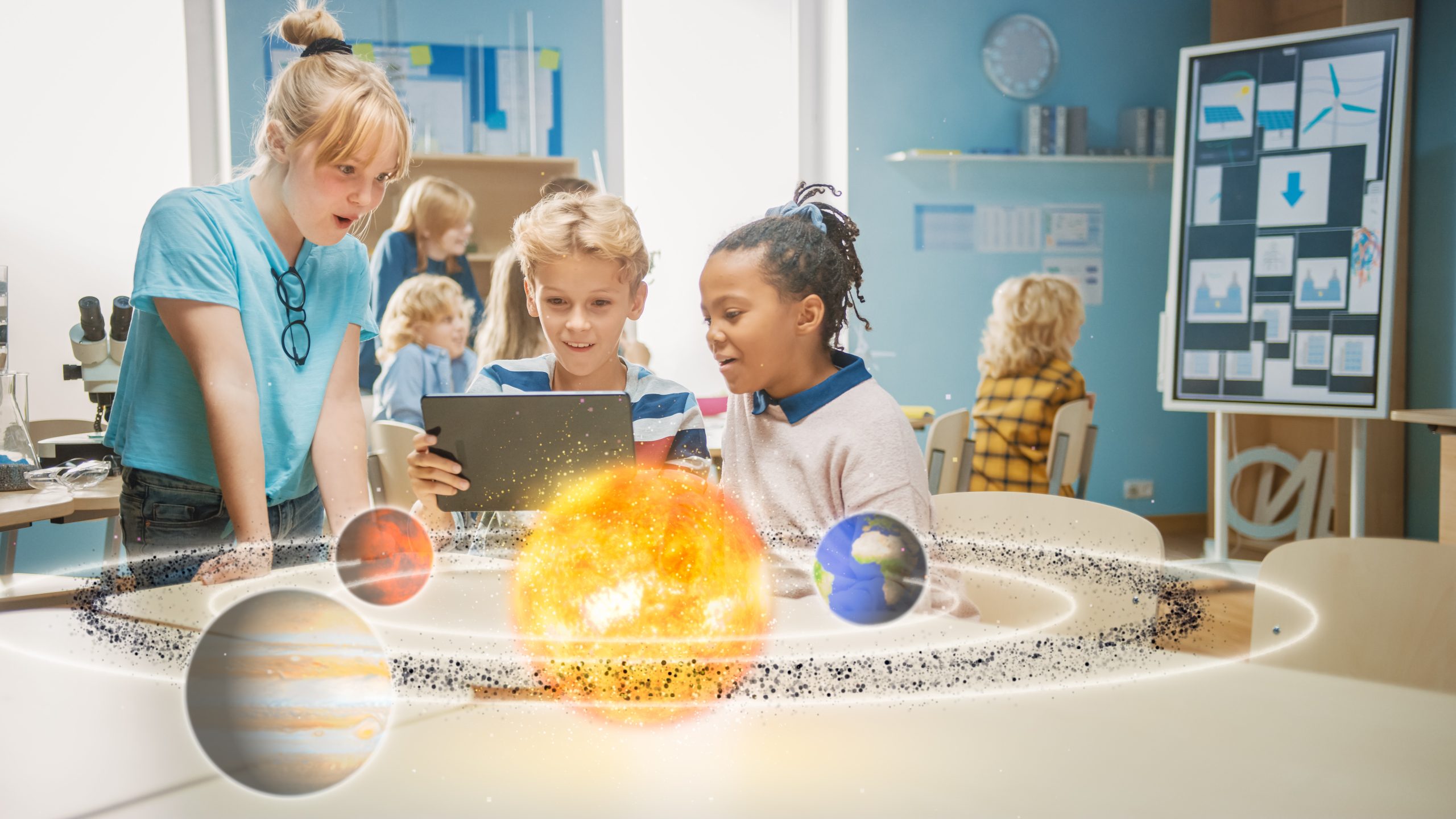 Three diverse school children using a digital tablet in science class to explore a 3D animation of the solar system through augmented reality.