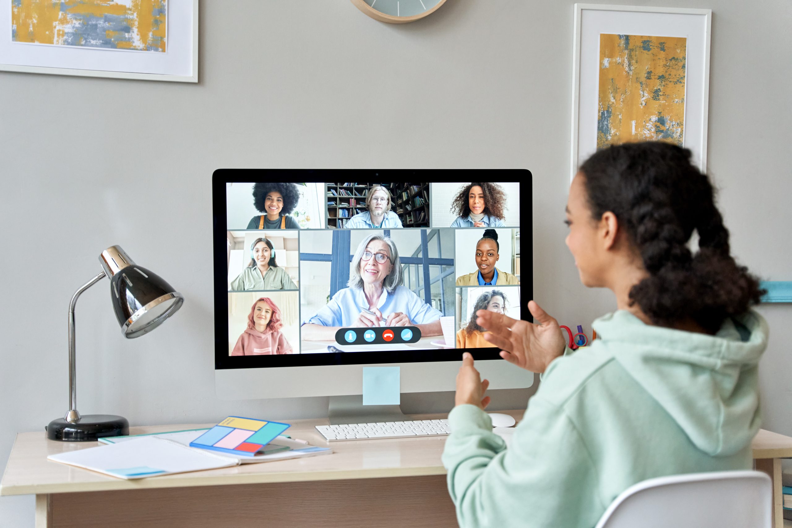 African teen girl engaged in a virtual class, interacting with her teacher and classmates on a computer screen from home.