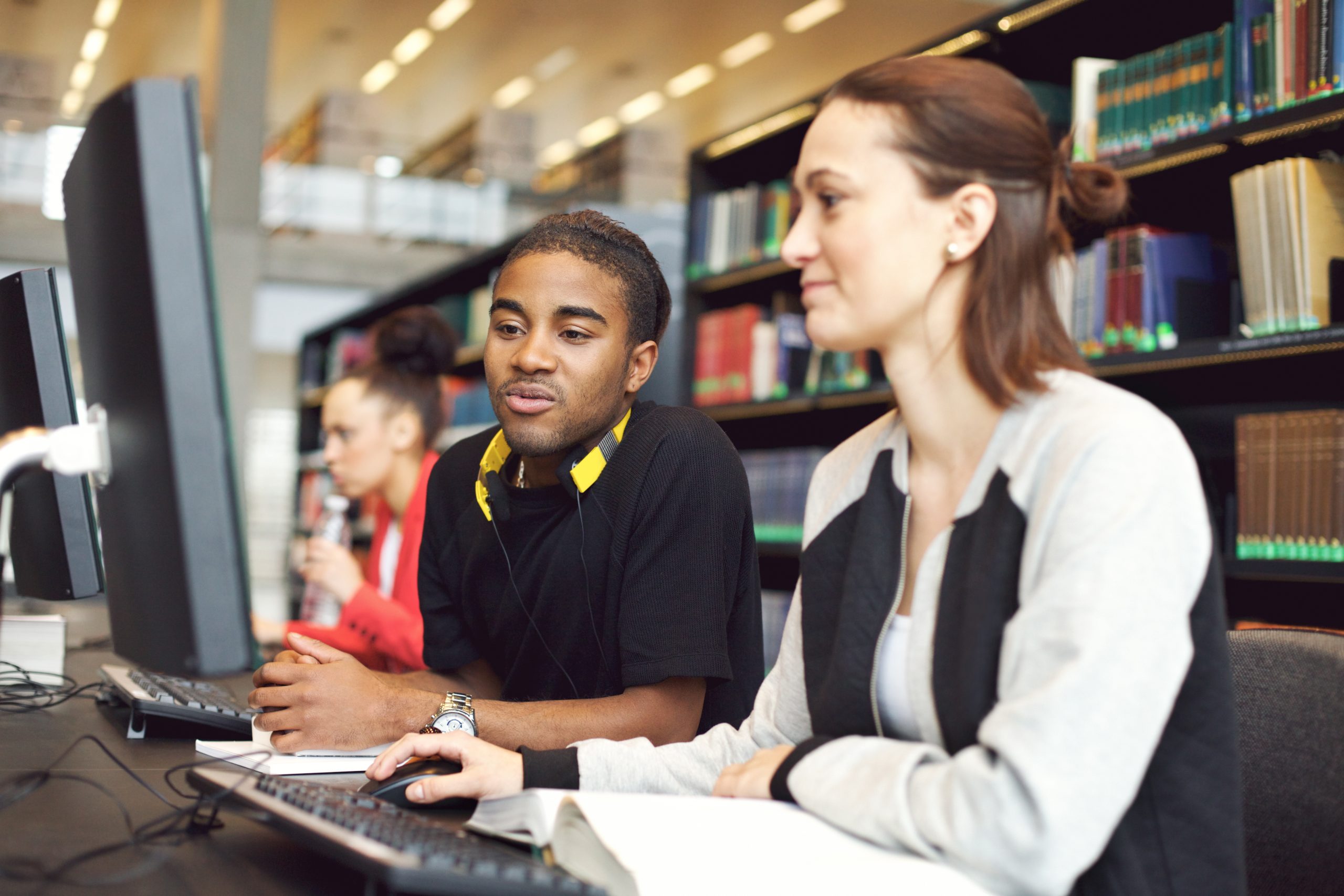 Young university students at a table, researching using computers in a modern library setting demonstrating the latter of Erikson's four stages.