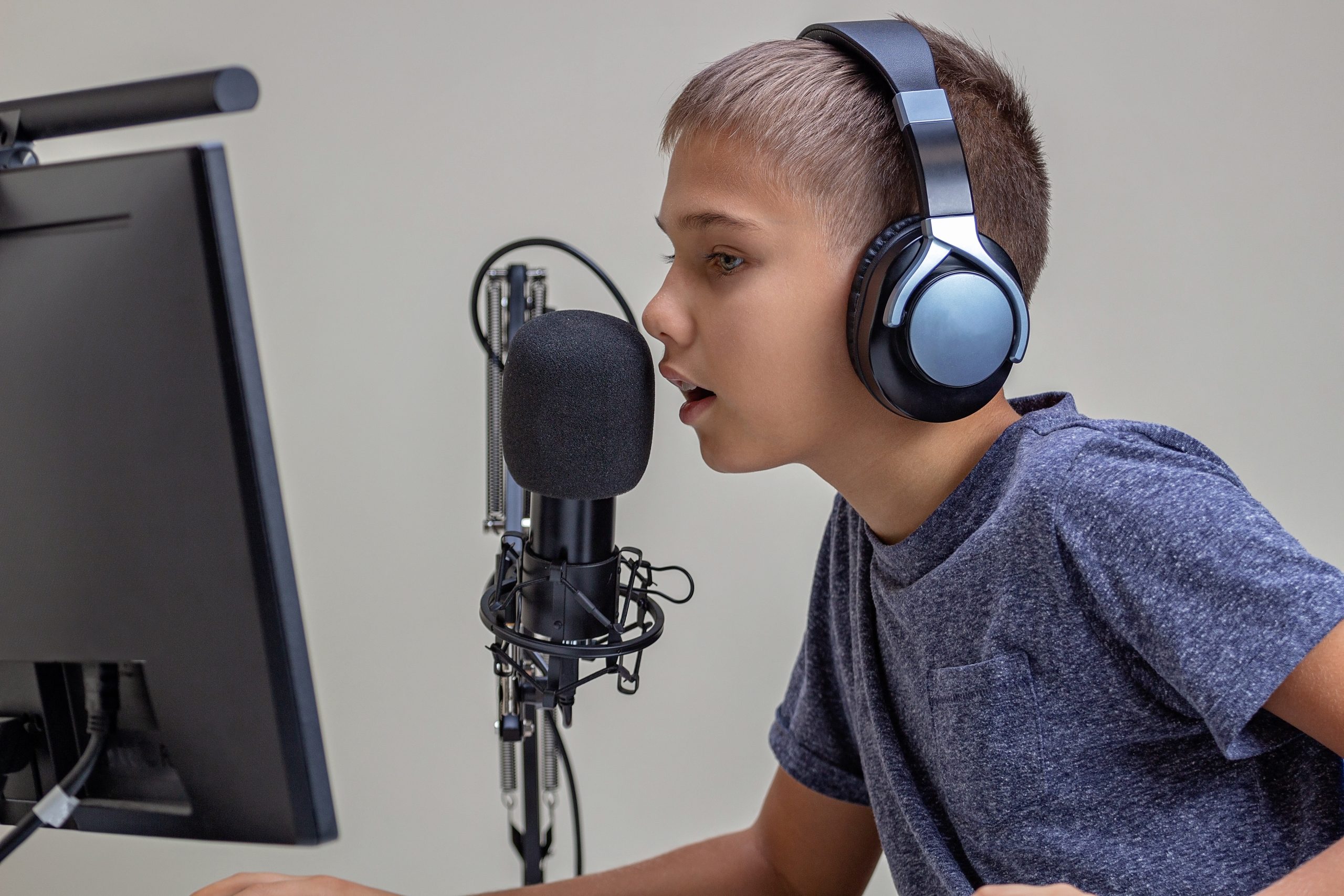 Boy with headphones and microphone engaged in a podcast production, staring intently at a computer monitor.