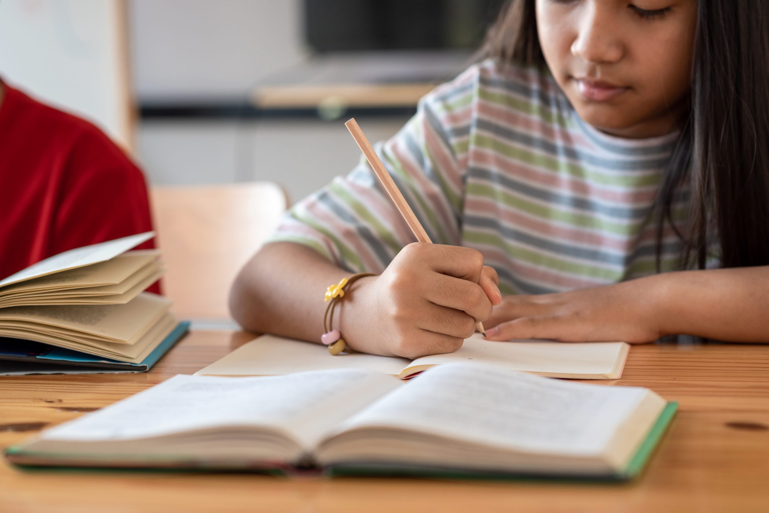 Girl in classroom setting, focused on her notebook as she writes down points from the teacher's lecture, embodying the Read/Write learning style from the VARK model.