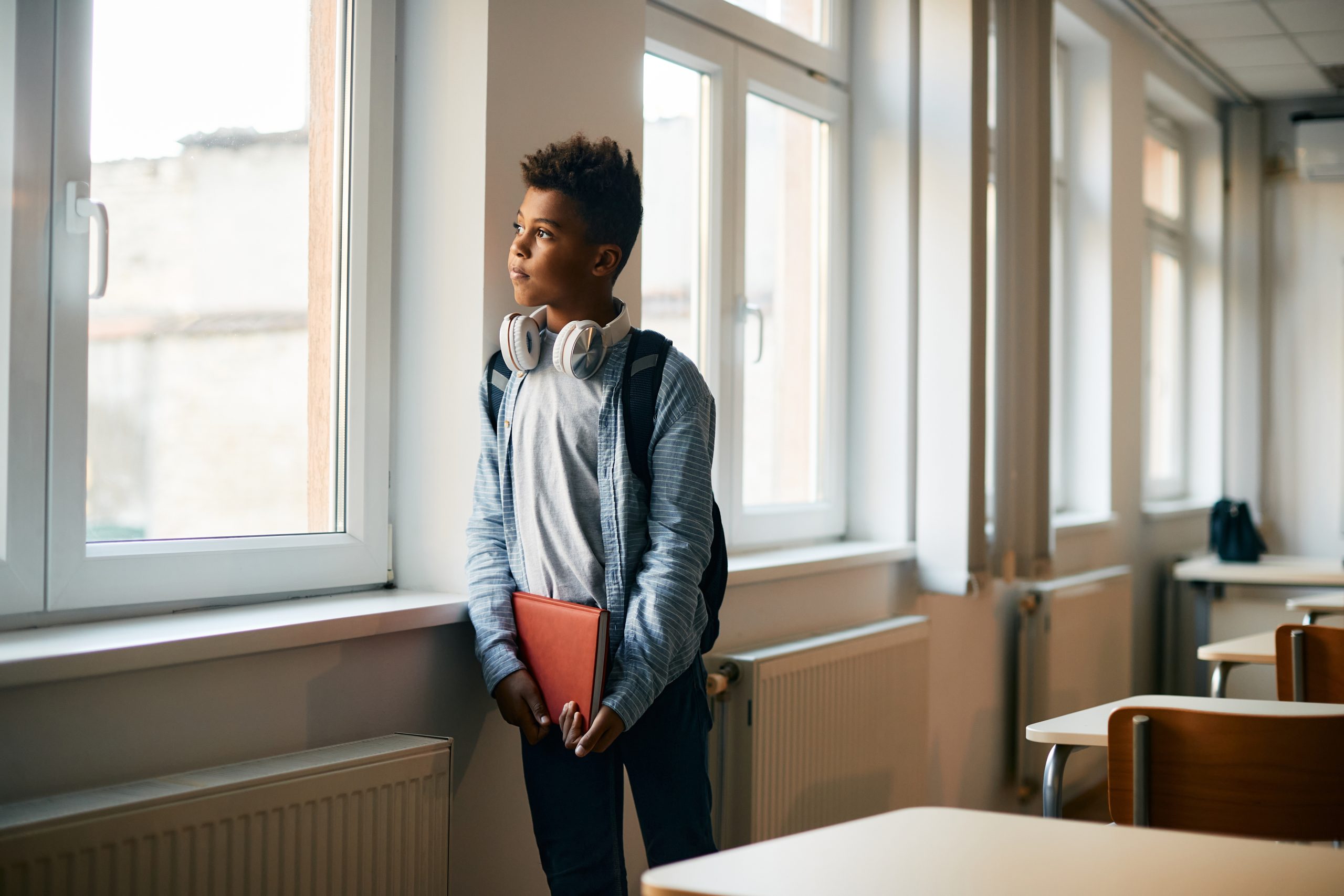 African American elementary student gazing thoughtfully out of a classroom window.