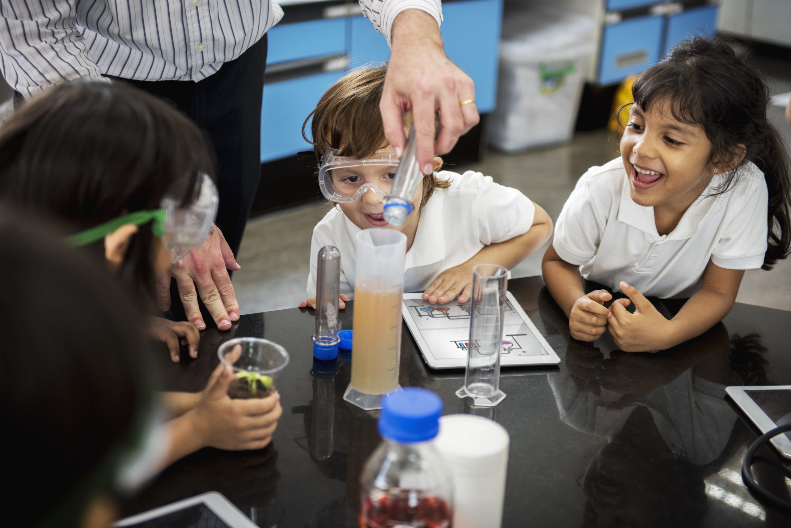 Diverse group of kindergarten students engaged in a science class, interacting with educational materials and listening to their teacher.