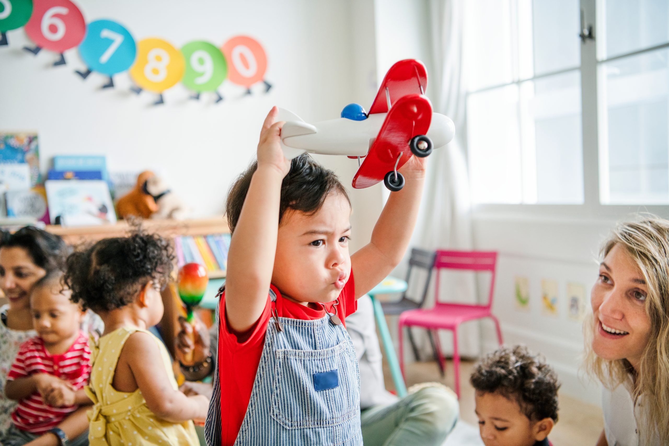 Preschooler smiling and holding an airplane toy, simulating flight.