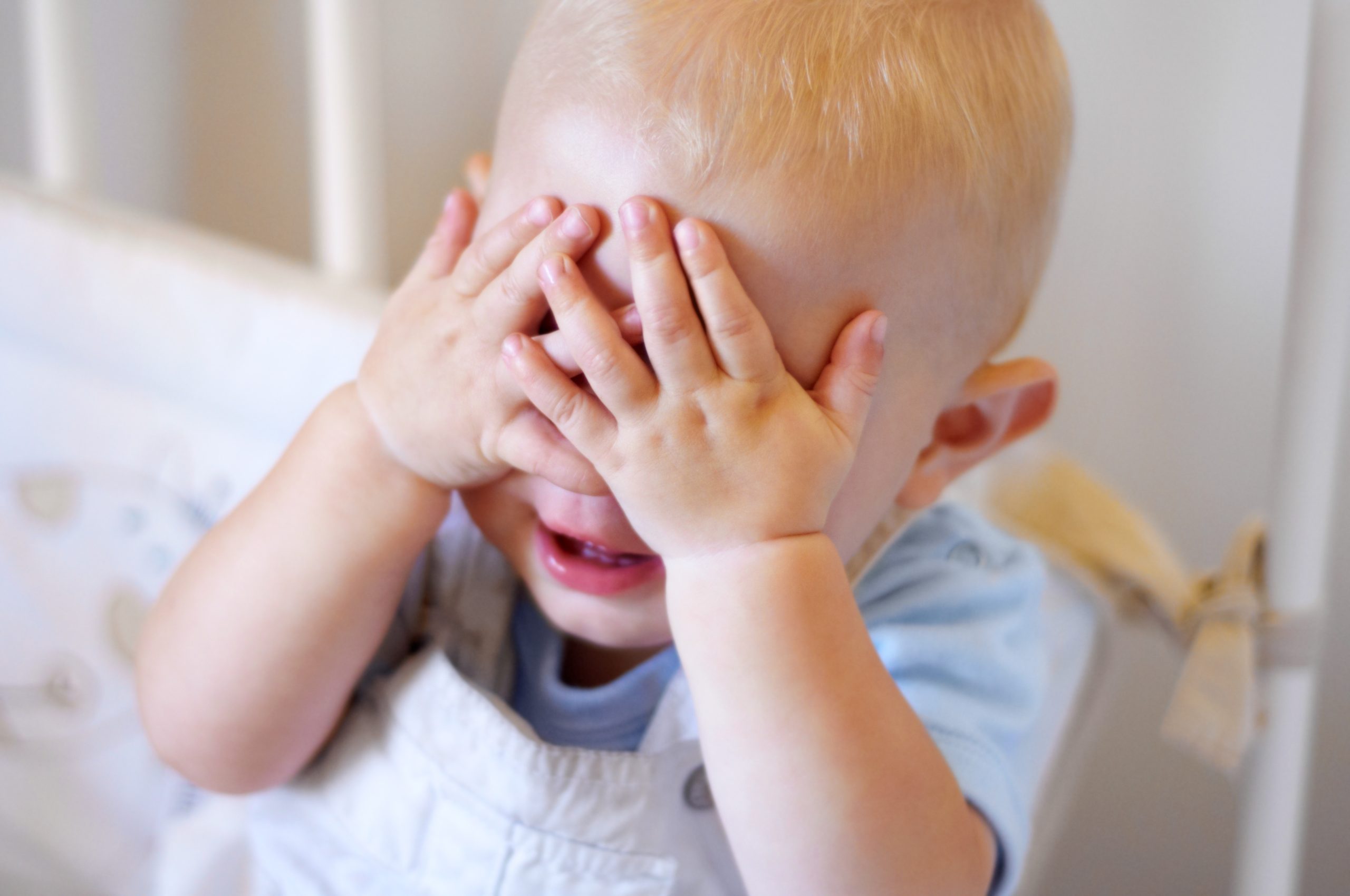 Baby boy playing peek-a-boo, covering his eyes with his small hands represents childhood egocentrism.