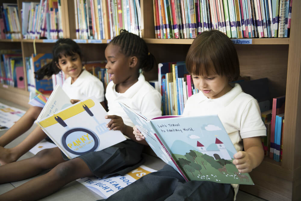 Children sit in a library, reading for enjoyment, demonstrating intrinsic motivation.