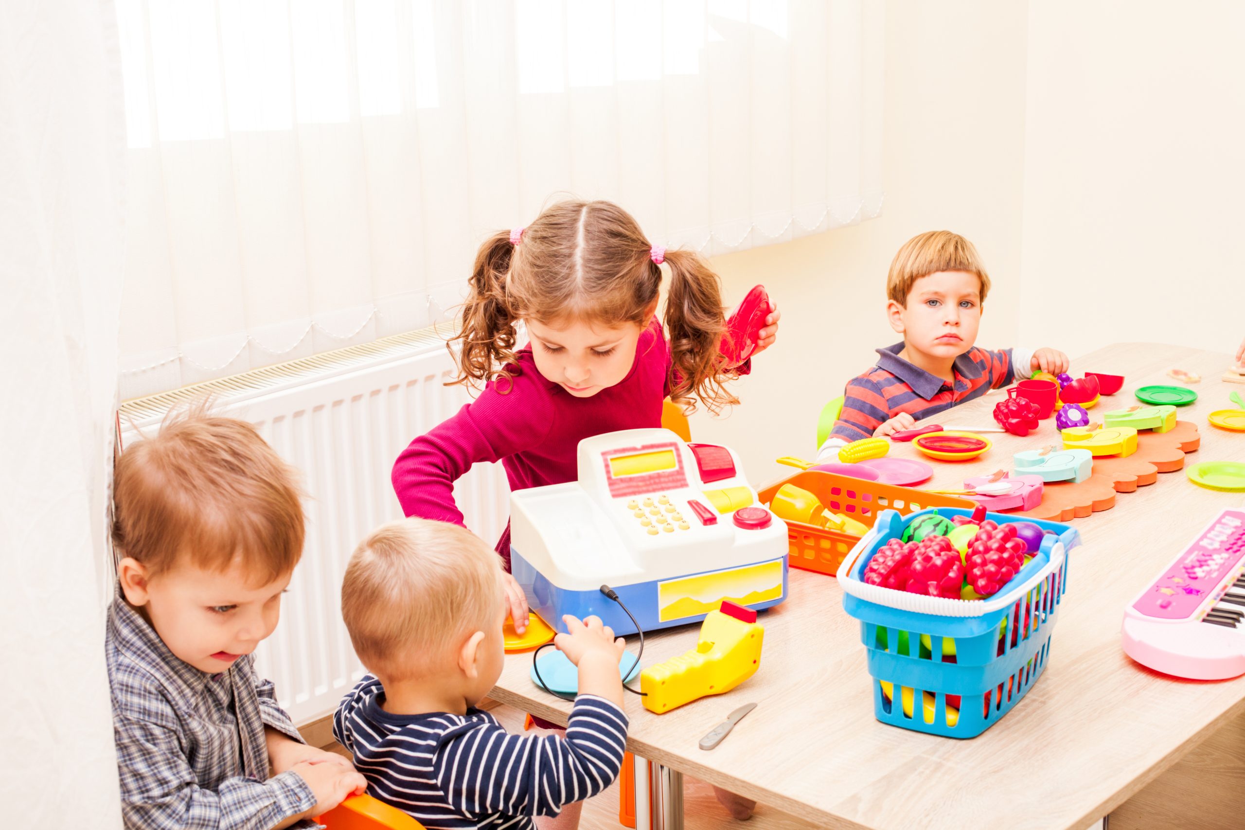 Group of children engaged in symbolic play, pretending to operate a shop with various items and play money.