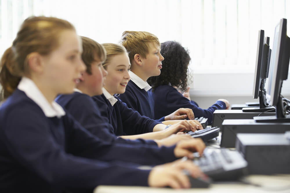 A row of uniformed pupils at computers use technology in education.